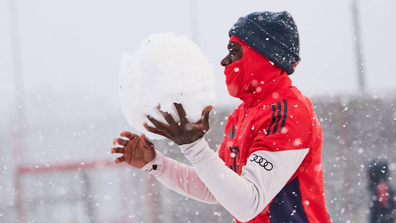 Alphonso Davies hält im Schneetreiben an der Säbener Straße einen großen Schneeball in der Hand