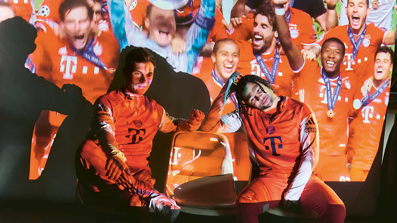 Joshua Kimmich und Serge Gnabry beim TV-Abend - auf einer Leinwand hinter ihnen sind Ausschnitte großer Bayern-Triumphe zu sehen