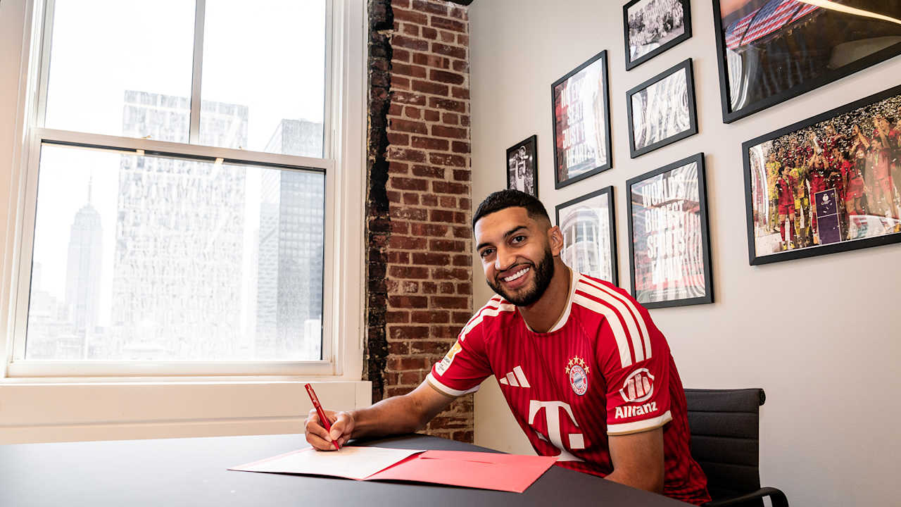 Ismael Saibari unterschreibt lächelnd im roten FC Bayern-Trikot ein Vertragspapier