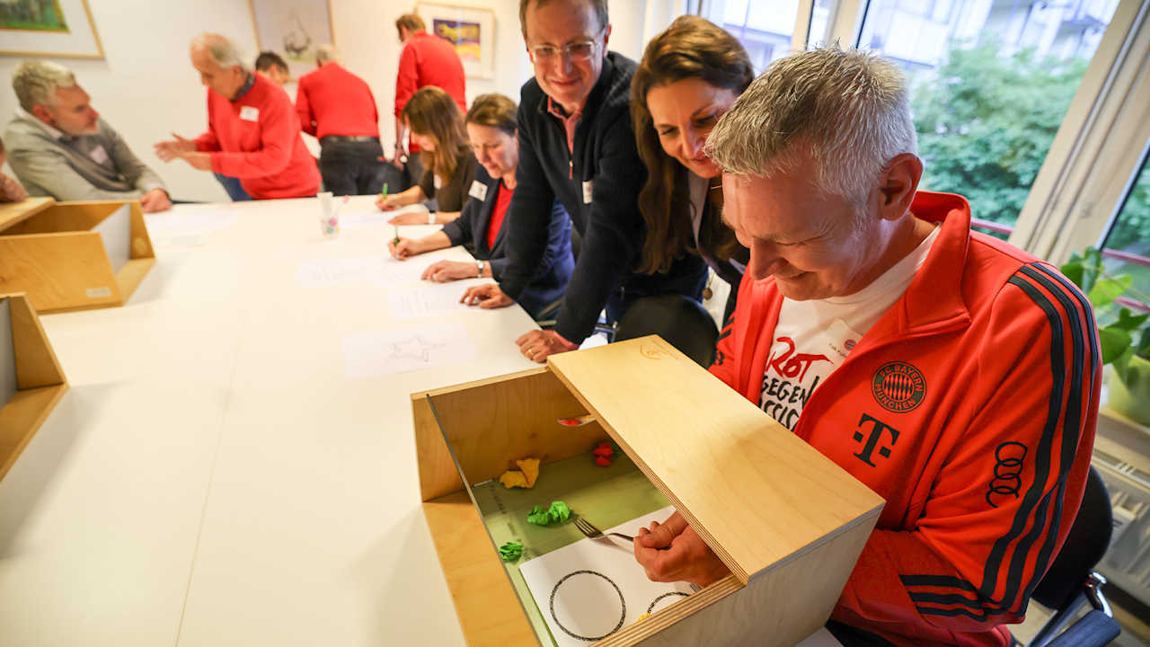 Eine Teilnehmer eines Workshops für Demenzhelfer beim FC Bayern absolviert eine Geschicklichkeitsaufgabe in einer verdeckten Kiste
