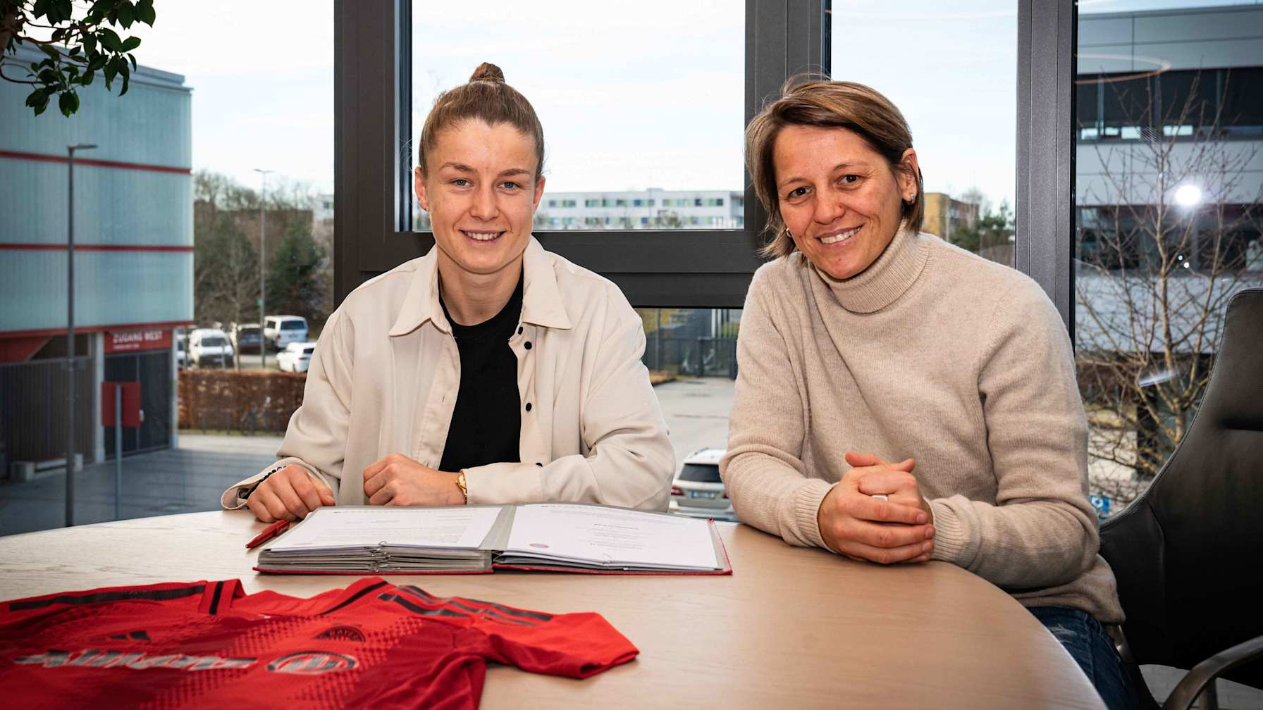 Bianca Rech und Michelle Ulbrich lächeln bei der Vertragsunterschrift in die Kamera.