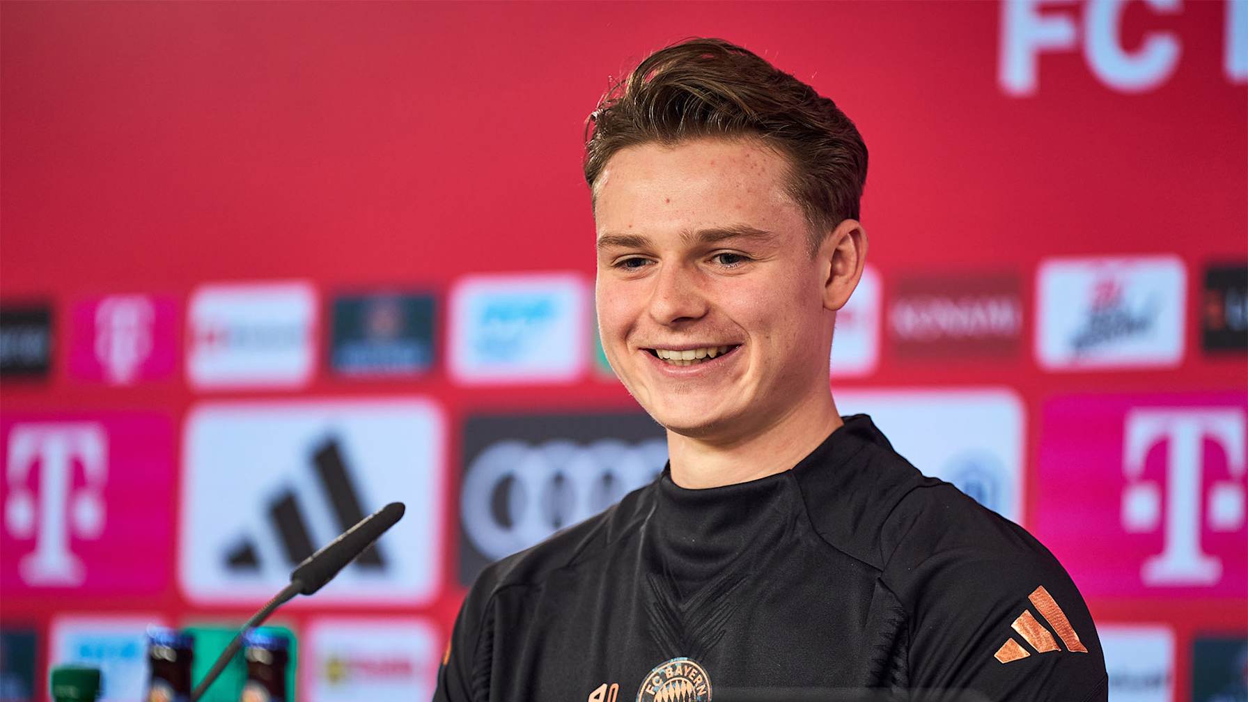 Jonas Urbig lächelnd auf seiner Vorstellungs-Pressekonferenz beim FC Bayern
