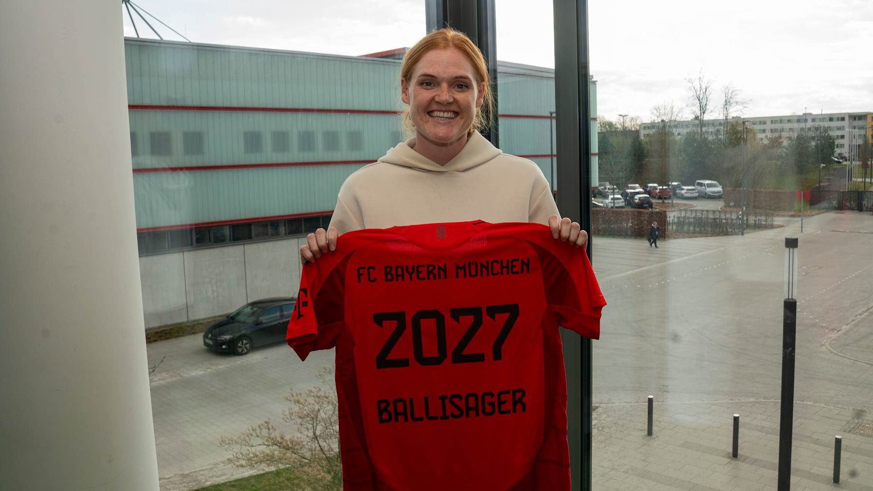 Stine Ballisager hält lächelnd das FC Bayern Trikot mit ihrem Namen und der Vertragslaufzeit in die Kamera.