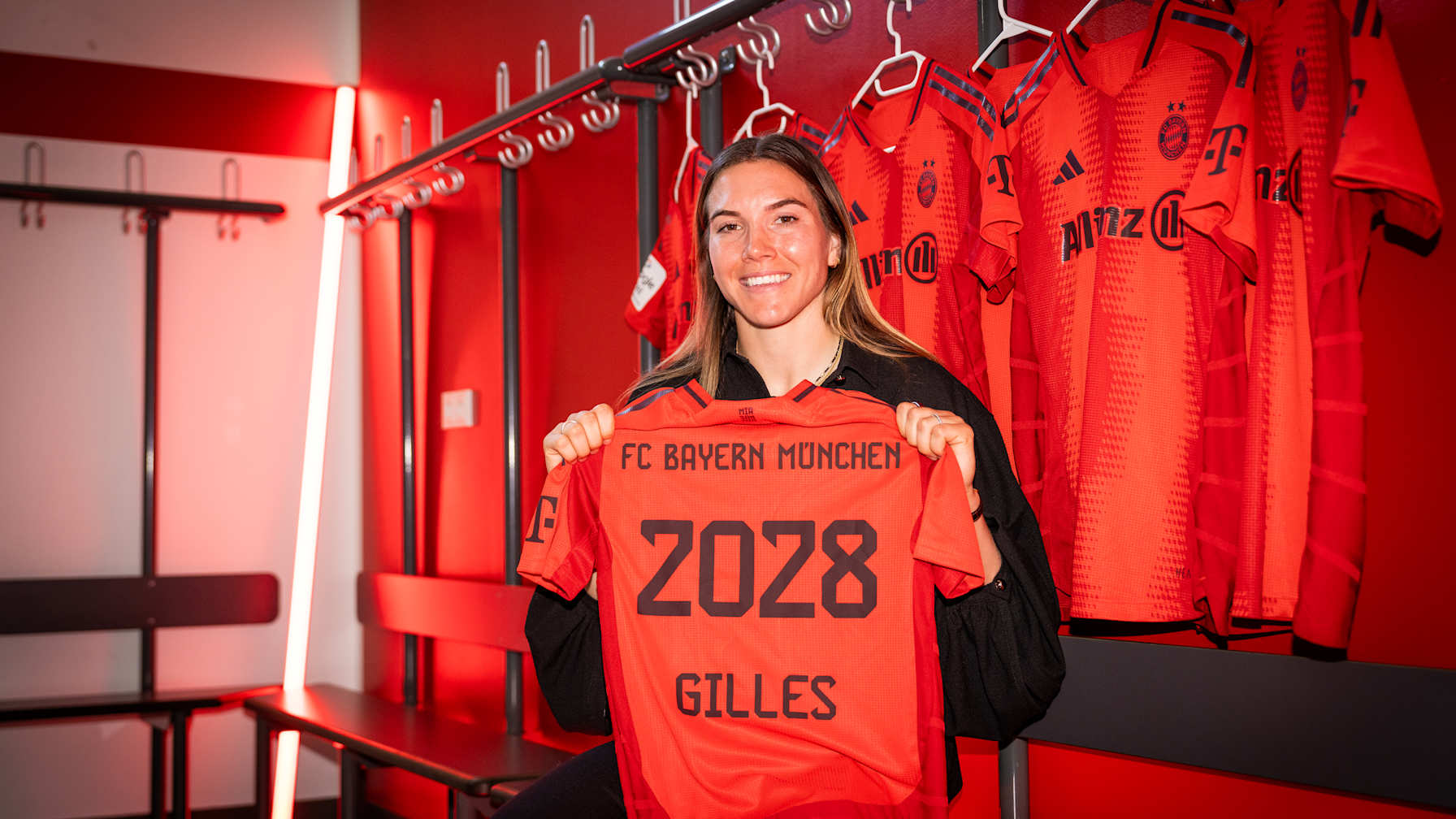 Vanessa Gilles smiles holding the FC Bayern shirt with her name and contract expiry year 2028.