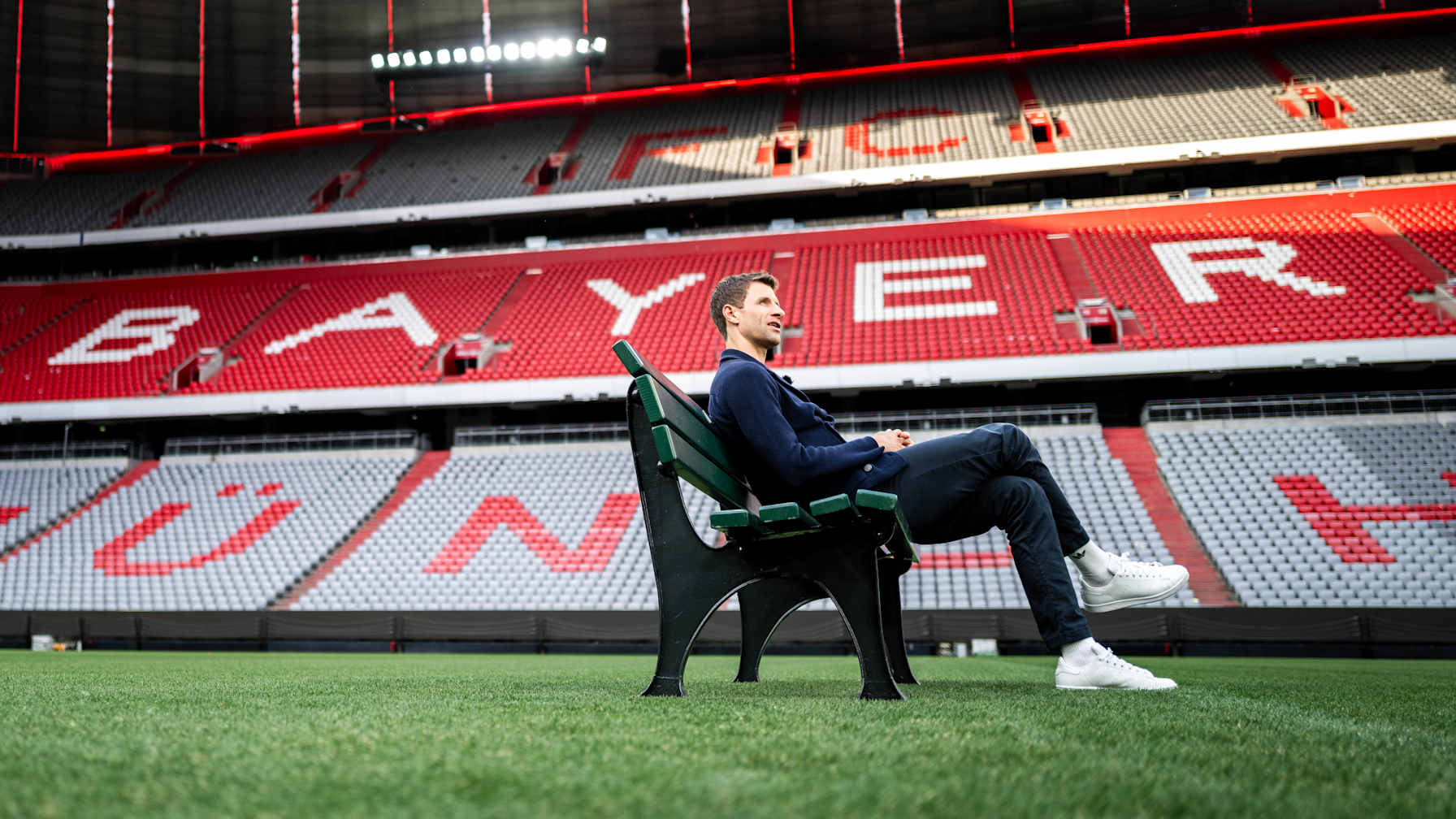Thomas Müller sits in the Allianz Arena on a park bench on the pitch.