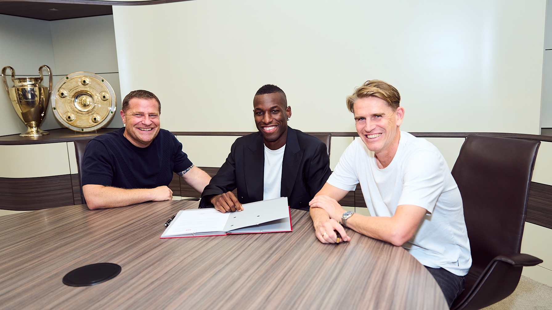 Max Eberl, Nicolas Jackson, Christoph Freund sitzen an einem Tisch, Jackson unterschreibt einen Vertrag