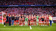 FC Bayern Women in a group photo in front of the Südkurve at the Allianz Arena with fans in the background.