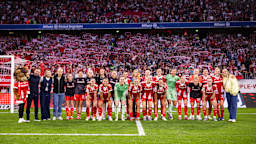 Die FC Bayern Frauen in einem Gruppenfoto vor der Südkurve der Allianz Arena mit Fans im Hintergrund.