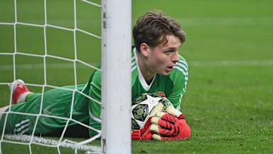 Torhüter Jonas Urbig liegt auf dem Rasen mit dem Ball in den Armen