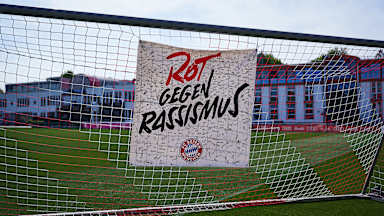 Ein Plakat mit Rot gegen Rassismus hängt in einem Tornetz auf dem Platz an der Säbener Straße