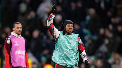 Michael Olise vom FC Bayern deutet beim Aufwärmen im Celtic Park nach oben.
