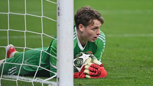 Goalkeeper Jonas Urbig lies on the turf with the ball in his arms