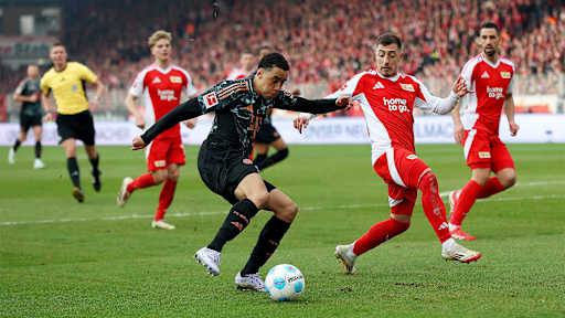 Jamal Musiala von Bayern München läuft mit dem Ball im Strafraum und wird von Josip Juranovic vom 1.FC Union Berlin bedrängt.