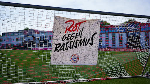 Ein Plakat mit Rot gegen Rassismus hängt in einem Tornetz auf dem Platz an der Säbener Straße