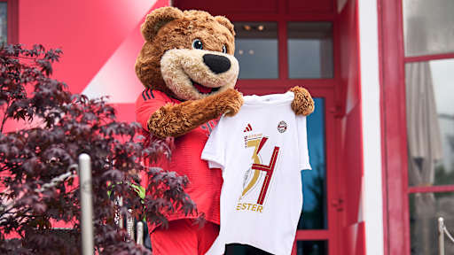 Maskottchen Berni hält das Meister-T-Shirt 2025 des FC Bayern hoch.
