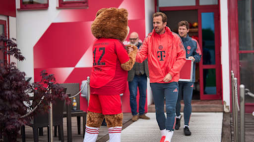 Harry Kane schlägt beim Betreten des Trainingsplatzes mit FC Bayern-Maskottchen Berni ein.