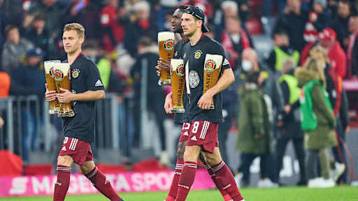 Joshua Kimmich und Leon Goretzka laufen mit je zwei Weißbiergläsern in den Händen über den Rasen.