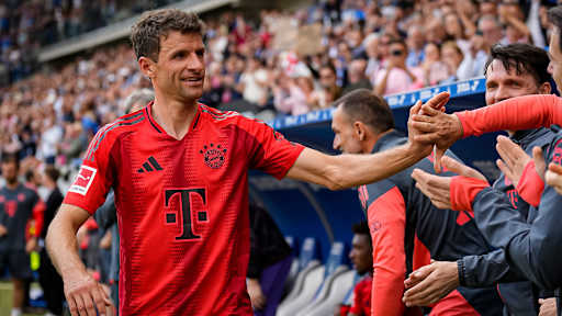Thomas Müller klatscht mit Mitspielern und Trainern auf der Auswechselbank des FC Bayern ab