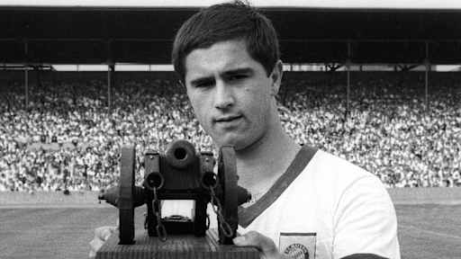 Gerd Müller betrachtet die Torjägerkanone, die er überreicht bekommen hat.