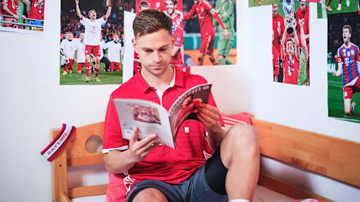 Joshua Kimmich sitzt in einem FC Bayern-Trikot in einem Kinderbett mit Bayern-Bettwäsche in einer Nachbildung eines Thomas Müller-Kinderzimmers.