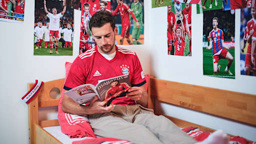 Leon Goretzka sitzt in einem FC Bayern-Trikot in einem Kinderbett mit Bayern-Bettwäsche in einer Nachbildung eines Thomas Müller-Kinderzimmers.