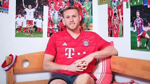 Daniel Peretz sitzt in einem FC Bayern-Trikot in einem Kinderbett mit Bayern-Bettwäsche in einer Nachbildung eines Thomas Müller-Kinderzimmers.
