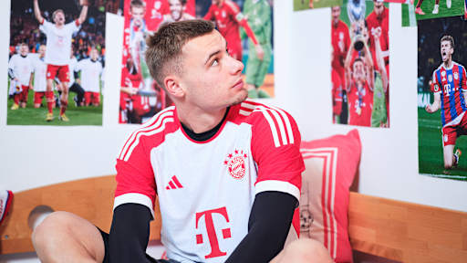 Gabriel Vidovic sitzt in einem FC Bayern-Trikot in einem Kinderbett mit Bayern-Bettwäsche in einer Nachbildung eines Thomas Müller-Kinderzimmers.