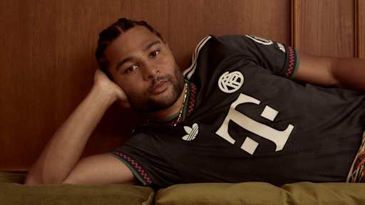 Serge Gnabry trägt das neue Champions League-Trikot des FC Bayern für die Saison 2025/26 in Schwarz mit roten, grünen und off-white Akzenten.