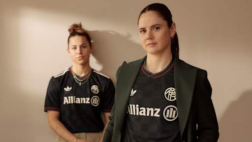 Sarah Zadrazil und Lena Oberdorf tragen das neue Champions League-Trikot des FC Bayern für die Saison 2025/26 in Schwarz mit roten, grünen und off-white Akzenten.