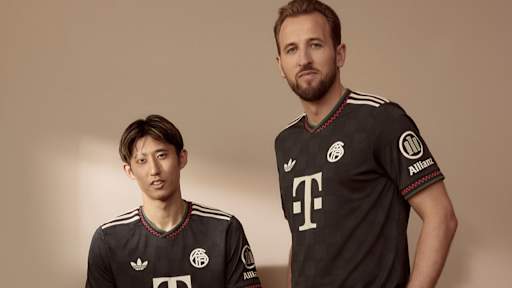 Hiroki Ito und Harry Kane tragen das neue Champions League-Trikot des FC Bayern für die Saison 2025/26 in Schwarz mit roten, grünen und off-white Akzenten.