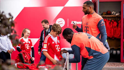Jonathan Tah und Dayot Upamecano unterschreiben auf dem FC Bayern-Trikot eines jungen Fans beim öffentlichen Training des FC Bayern
