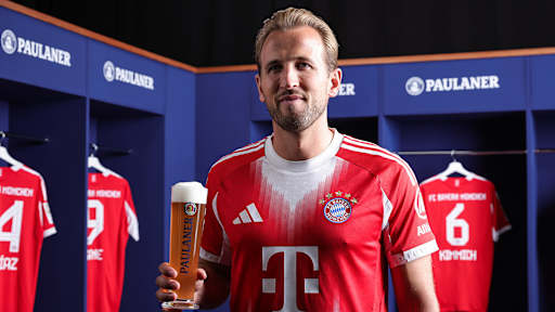 Harry Kane hält ein Glas Weißbier in der Hand und trägt ein FC Bayern-Trikot
