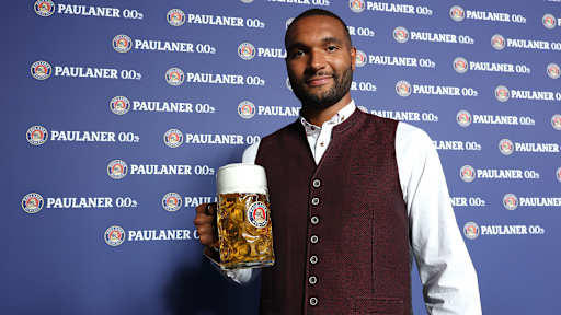 Jonathan Tah mit einem Maßkrug Bier vor einer Wand mit Paulaner-Schriftzug
