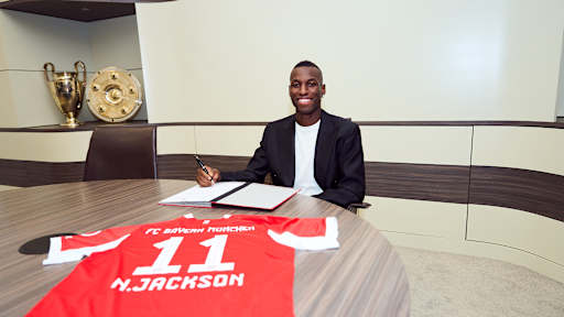 Nicolas Jackson sitzt an einem Tisch und unterschreibt den Vertrag beim FC Bayern