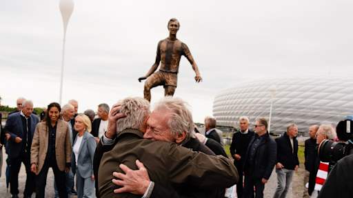 Paul Breitner umarmt jemanden vor der Statue von Franz Beckenbauer