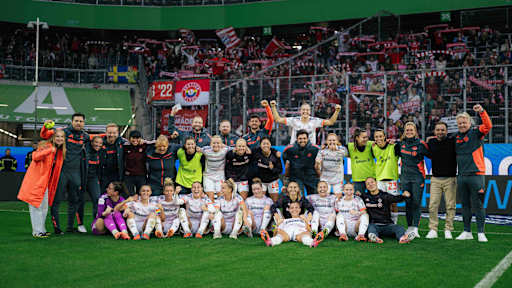Die jubelnde Mannschaft in einem Gruppenfoto vor dem FC Bayern Fanblock.