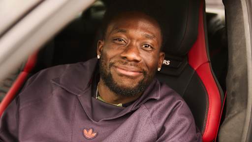 Alphonso Davies sitzt auf dem Fahrersitz seines Audi und lächelt
