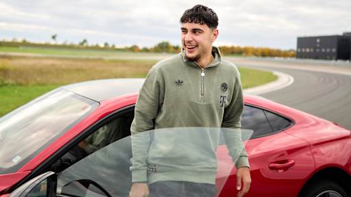 Aleksandar Pavlovic steeht lachend vor einem  roten Audi