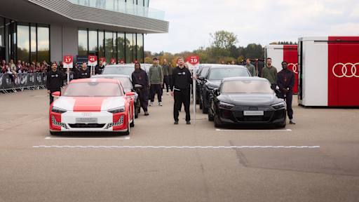 Spieler des FC Bayern stehen mit mehreren Audi-Fahrzeugen auf der Startlinie einer Rennstrecke