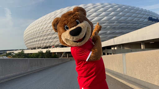 Berni steht vor der Allianz Arena und zeigt mit seinem Zeigefinger drauf.