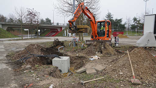 Ein Bagger gräbt ein Loch für die E-Ladesäule am E-Ladepark vor der Allianz Arena
