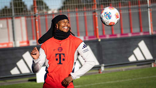 Michael Olise schaut einen Ball an und lacht im Training des FC Bayern