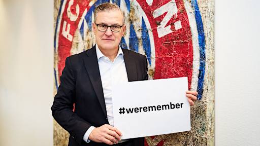Jan Christian Dreesen, Vorstandsvorsitzender des FC Bayern, zeigt mit ernster Miene ein Banner mit der Aufschrift "weremember" in die Kamera