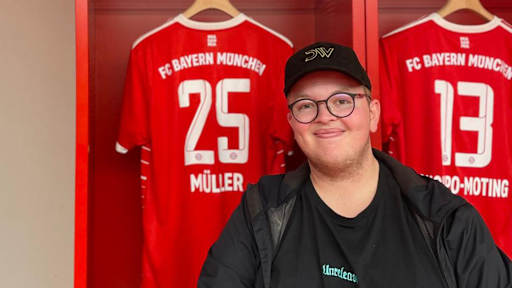FC Bayern-Fan Glenn sitzt in der Kabine der Allianz Arena vor einem Trikot von Thomas Müller