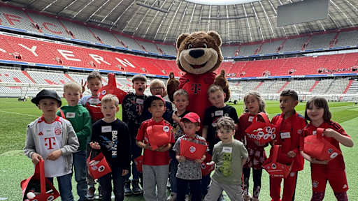 Berni und KIDS CLUB-Kinder stehen mit ihrem Osternest auf dem Rasen der Allianz Arena.
