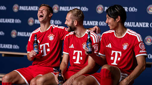 Joshua Kimmich, Konrad Laimer und Hiroki Ito unterhalten sich und lachen im FCB-Trikot mit Paulaner Bier