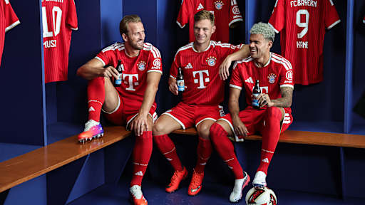Harry Kane, Joshua Kimmich und Luis Diaz sitzen in einer Kabine im FC Bayern Trikot und halten Paulaner Bier in der Hand