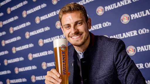 Josip Stanisic hält ein Paulaner Bier in der Hand und lacht