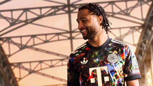 Serge Gnabry  trägt das neue FC Bayern-Wiesn-Trikot 2026/27 mit farbenfrohem floralen Muster, im Hintergrund ist die Münchner Hackerbrücke zu sehen