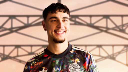 Aleksandar Pavlovic  trägt das neue FC Bayern-Wiesn-Trikot 2026/27 mit farbenfrohem floralen Muster, im Hintergrund ist die Münchner Hackerbrücke zu sehen